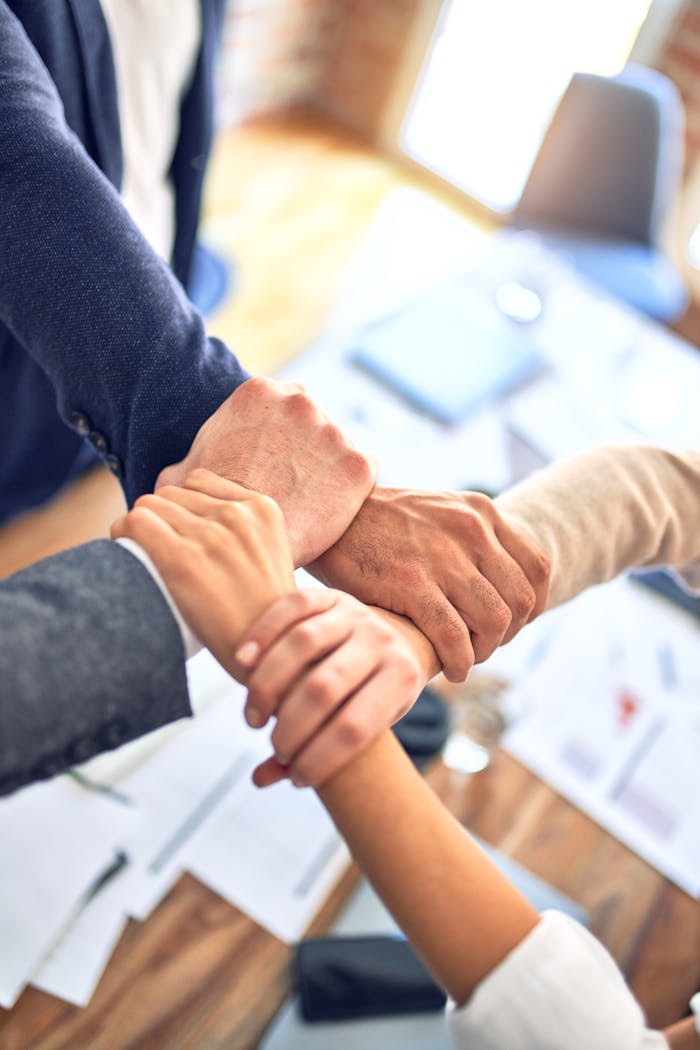 Close-up of diverse hands joining together over a table in an office setting, symbolizing teamwork and cooperation.